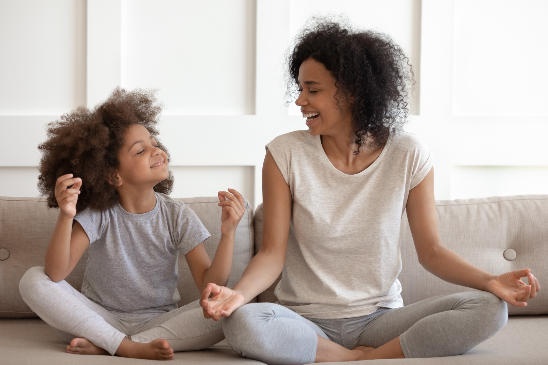 Mujer afroamericana emocionada practicando yoga con hija pequeña.